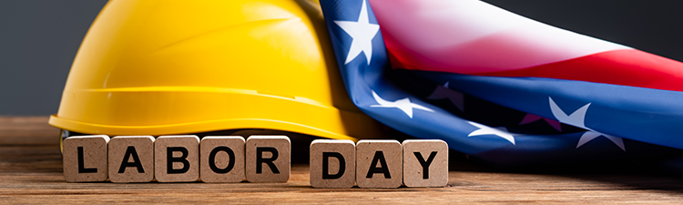 Yellow hard hat beside a folded American flag and wooden letter blocks spelling âLABOR DAY.â