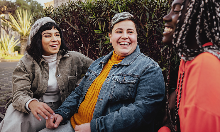 Three people sit outdoors together, smiling and talking.