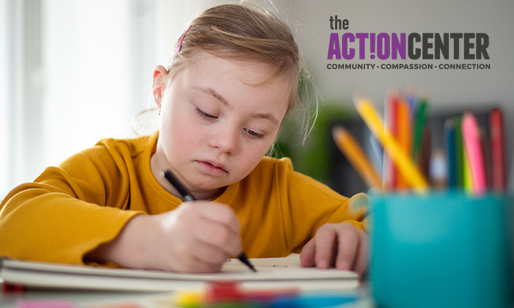 A young girl with Down syndrome wearing a yellow sweater draws with a pencil at a desk. The Action Center logo reads Community Compassion Connection.