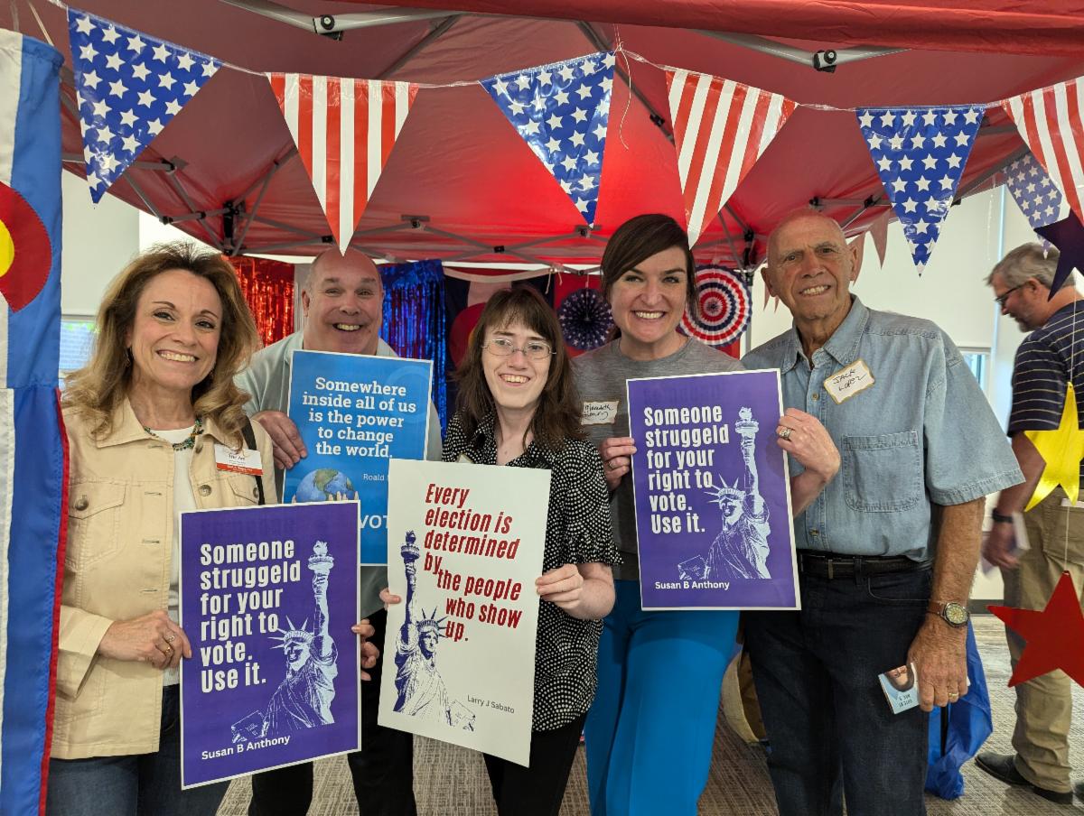 Five people pose under patriotic decorations holding signs encouraging people to vote.