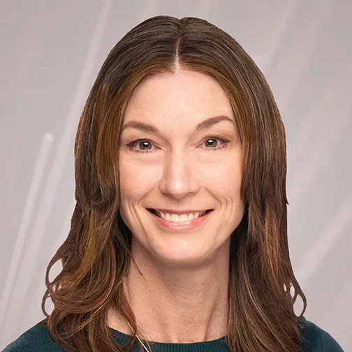 A smiling woman with long brown hair poses for a headshot against a light gray background.