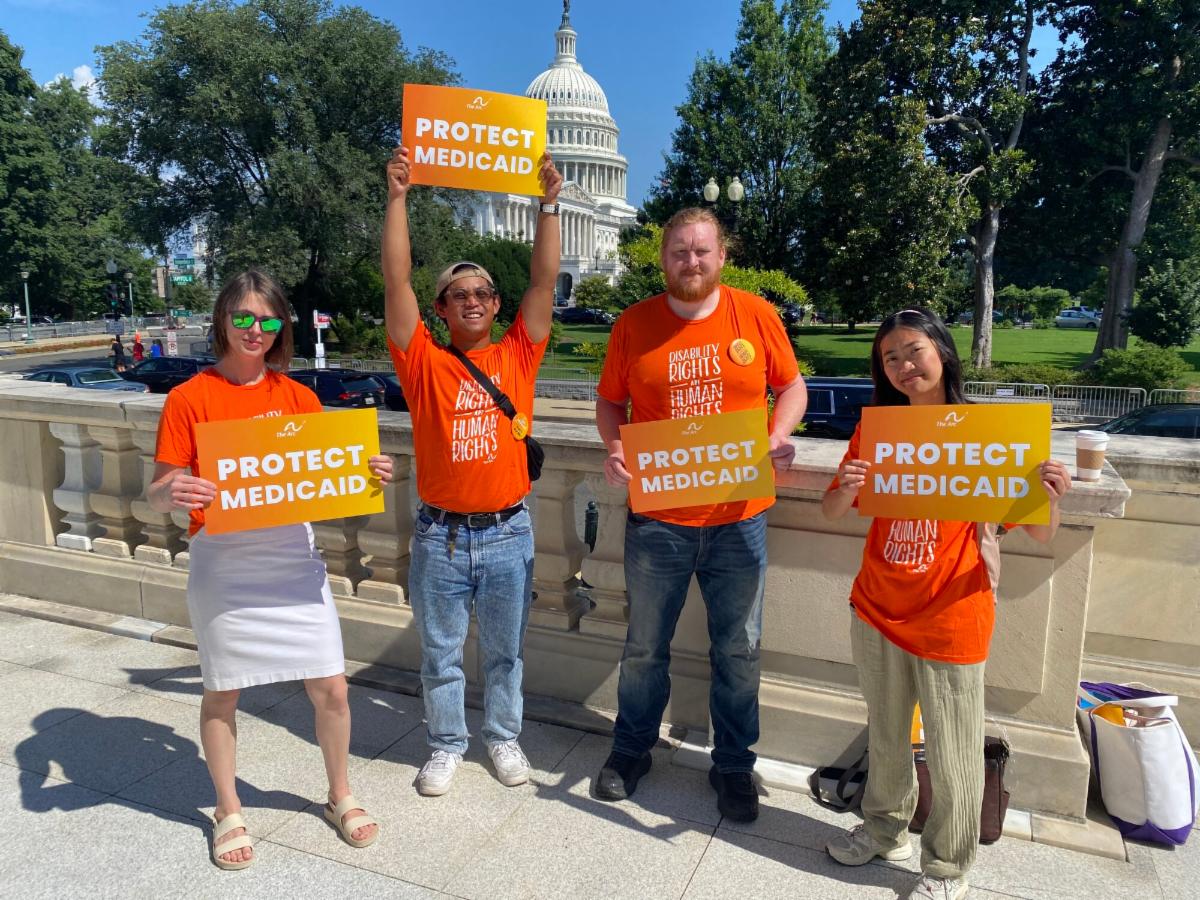 Four advocates in orange shirts hold Protect Medicaid signs outside the U.S. Capitol