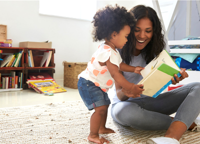 Mother and toddler look at a book together with a bookshelf with more books in background