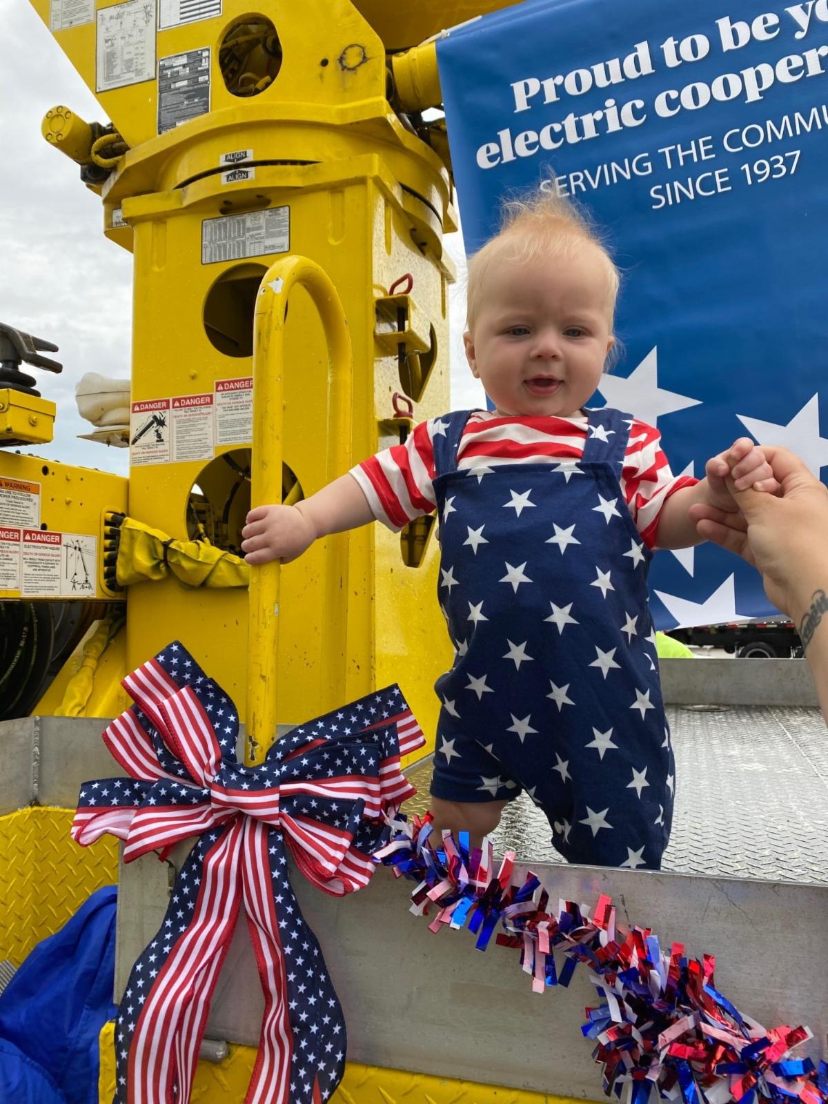 A small child in blue overalls with stars and a red and white striped shirt stands on a WH truck
