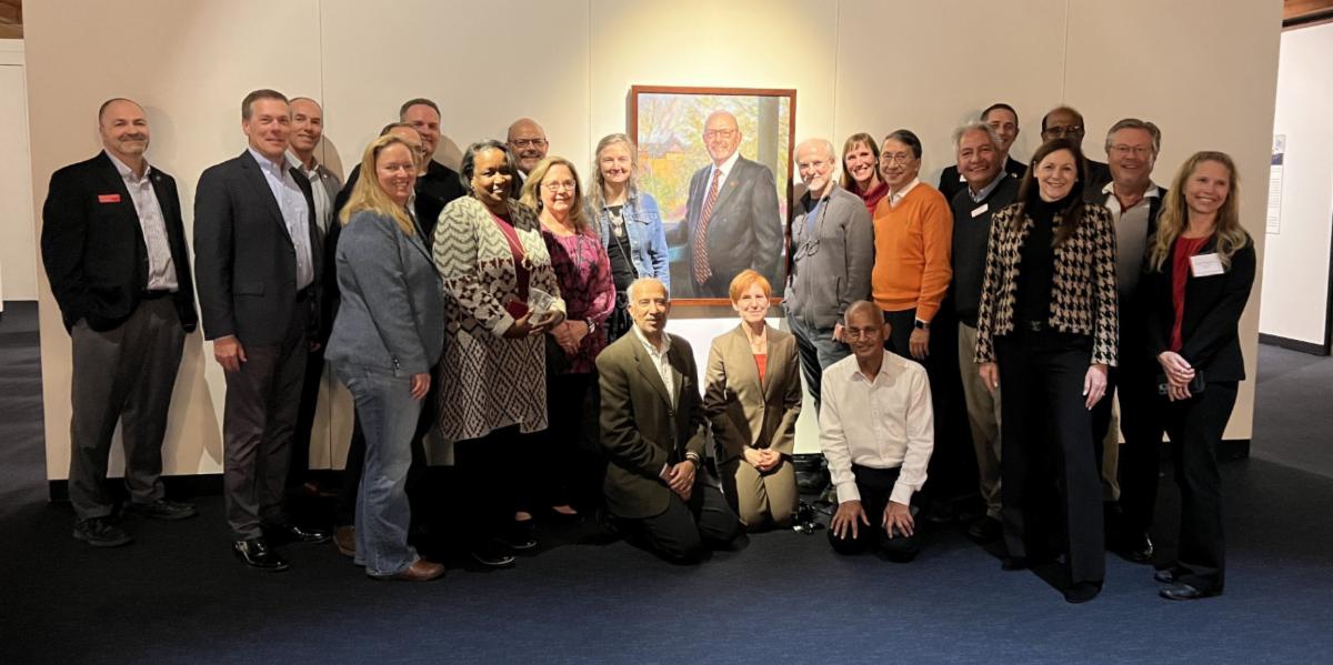 Group photo of people surrounding a painted portrait on display