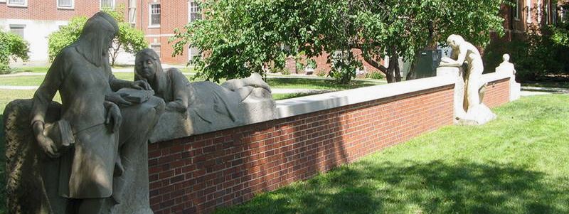 Photo of outdoor sculpture called Conversations. Life sized people at a low brick wall. The sculpture people are sitting on or laying on or leaning against the wall engaged in conversations or reading