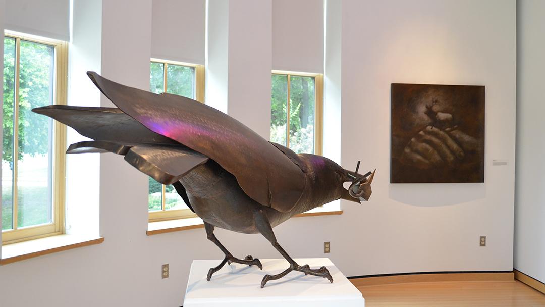 Photo of a large metal sculpture of a crow with artwork in the background