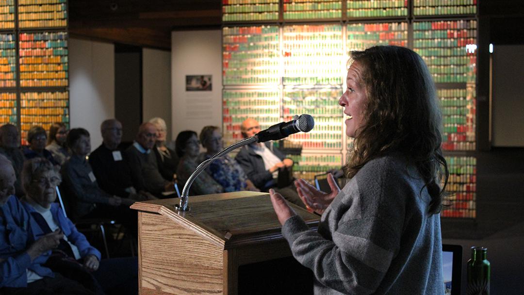 April Surgent in the Brunnier Art Museum at a podium with a crowd and her exhibition in the background