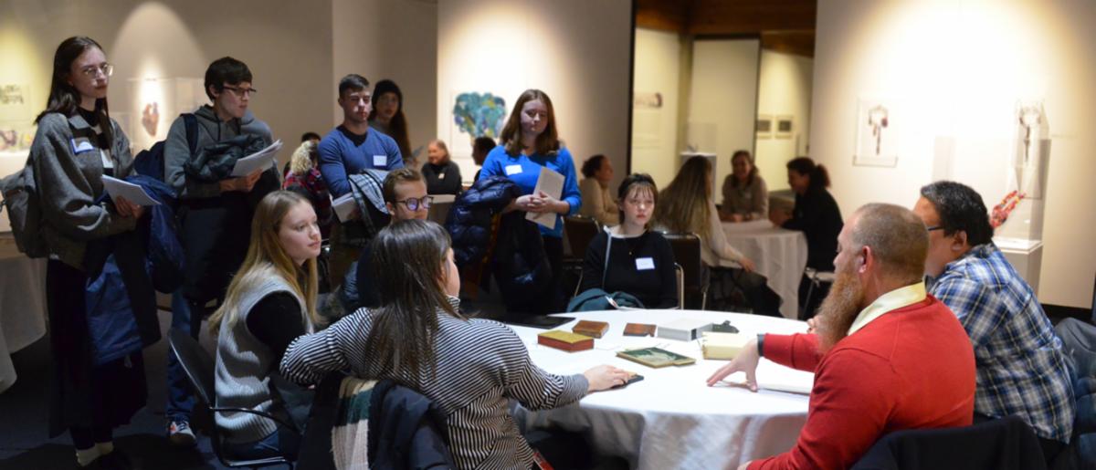 Professionals mingling with students sitting and standing at covered tables in Brunnier Art Museum