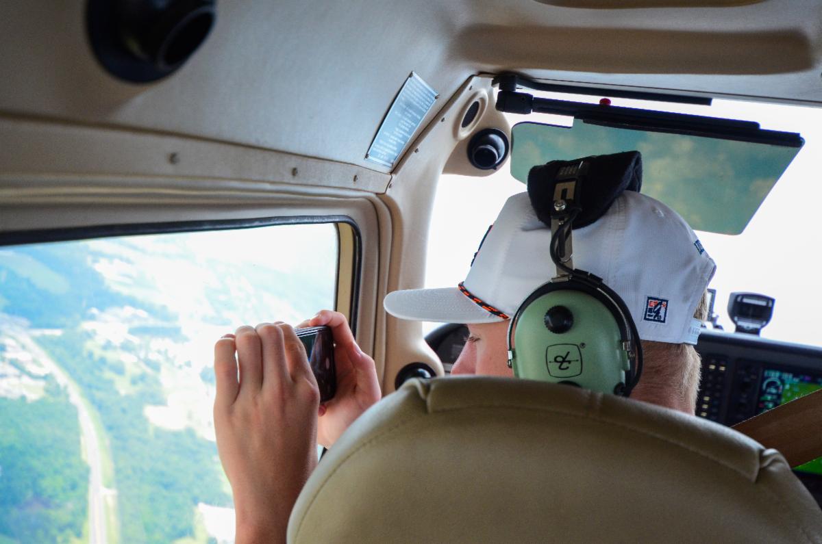 A young boy is taking pictures of Auburn Campus while sitting in the cockpit of a discovery flight.
