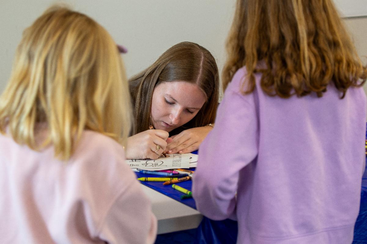 Student coloring a pilot for a day worksheet with two young girls in the foreground.