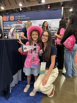 Taylor Deebs stands next to a young girl wearing "Girls in Aviation Day" merchandise as well as holding an Auburn Aviation flag.