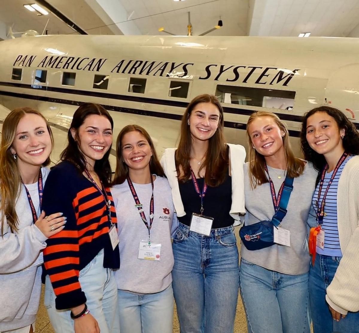 The two war eagle women teams are standing in front of a plane on display and smiling.