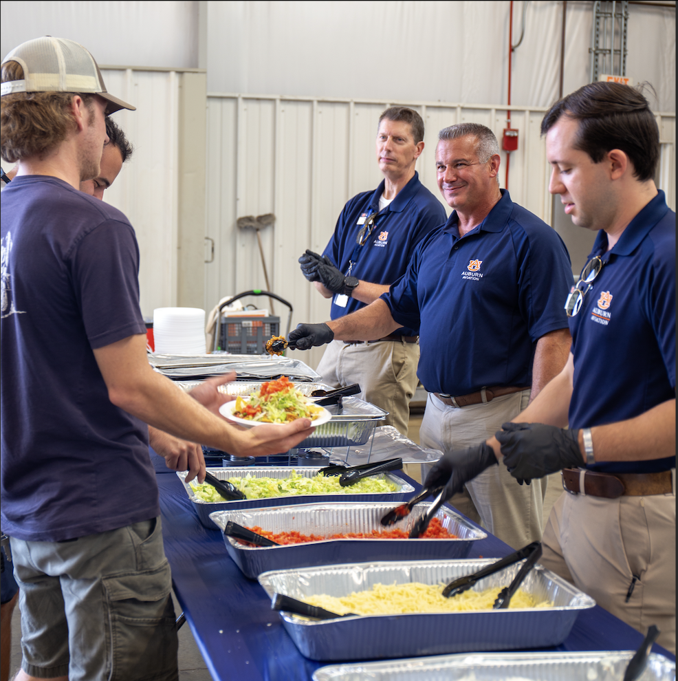 Three flight crew members serving food with smiles at the Welcome Back Lunch.