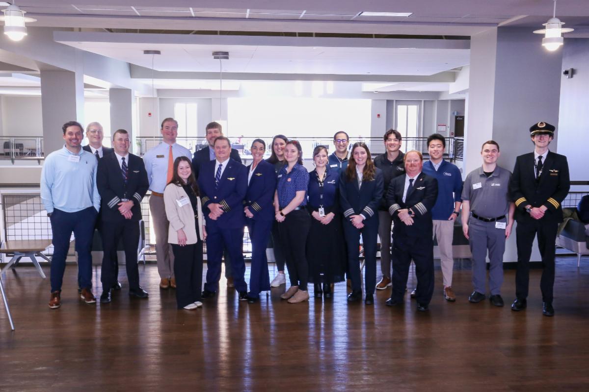 A group of aviation professionals stand inside the Melton Student Center while smiling at the camera.