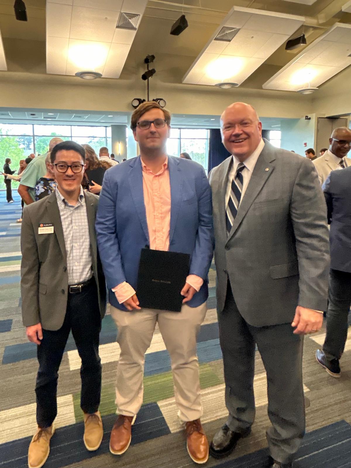 Max Yeast smiling at camera while holding an award. He is standing next to Auburn President Roberts and Professor Daniel Siao