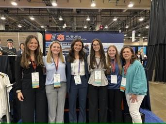 Six member of Women in Aviation War Eagle Chapter stand in front of an Auburn Aviation booth.