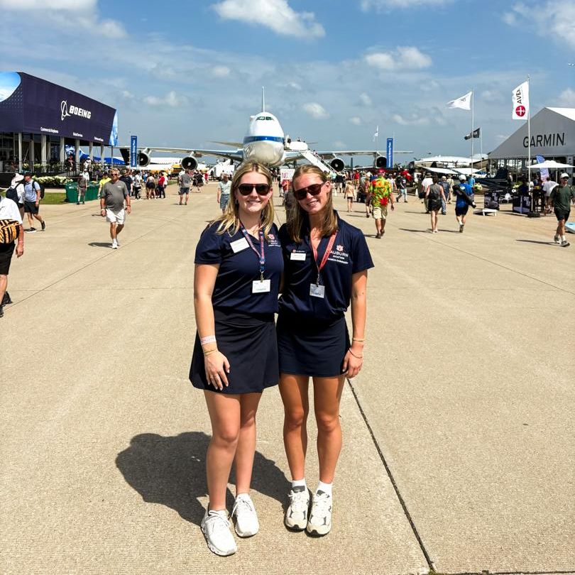 Two striped wing ambassadors stand in front of plane at Osh Kosh