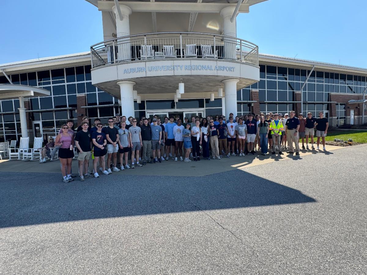 A group of students hold bags of trash in front of the Auburn University Regional Airport.