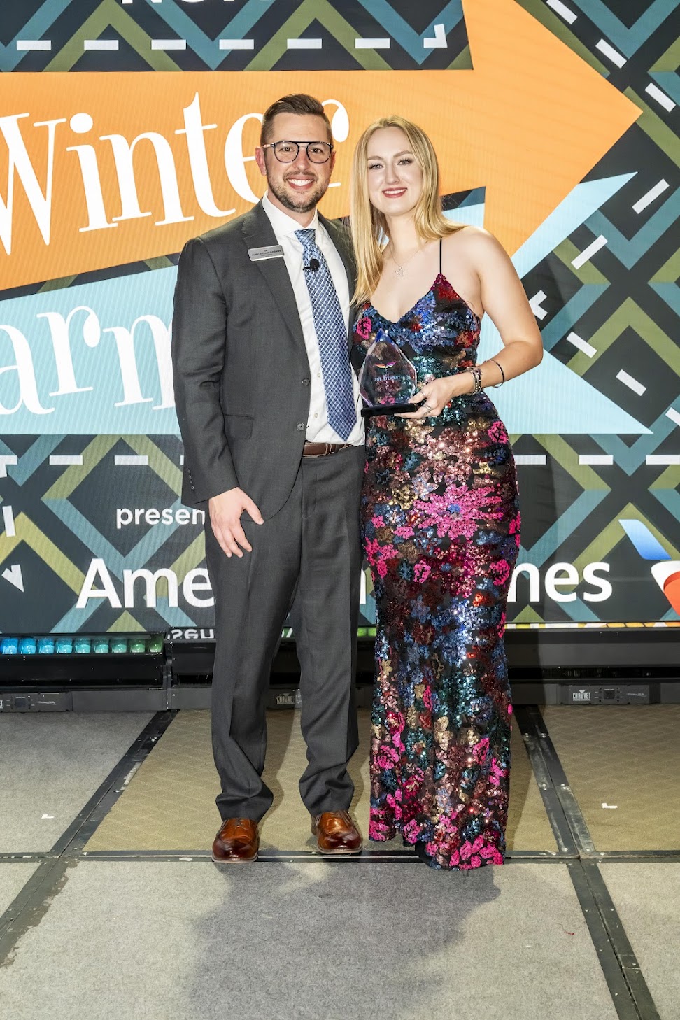 Zoe Stewart alongside an award presenter hold an award while smiling at the camera.