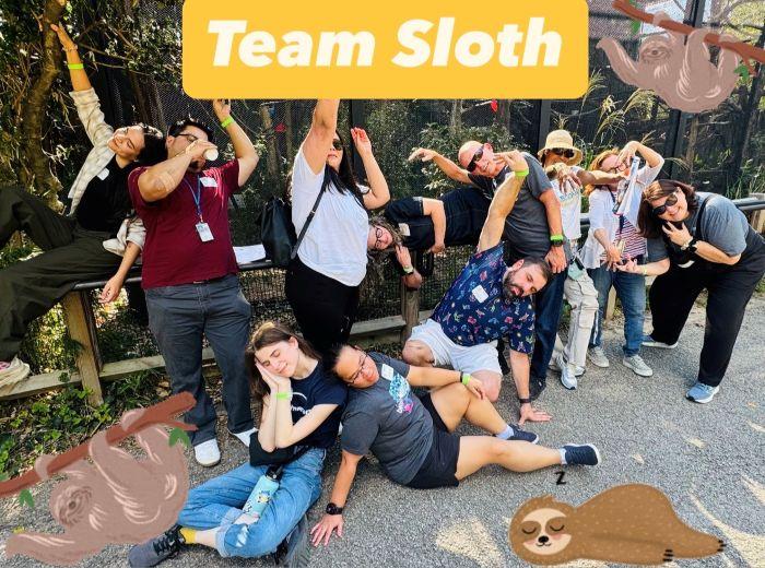 A group of faculty and staff poses lazily for a picture in front of the sloth enclosure as part of a teambuilding exercise