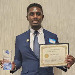 Dr Adedolapo holding certificate and glass trophy