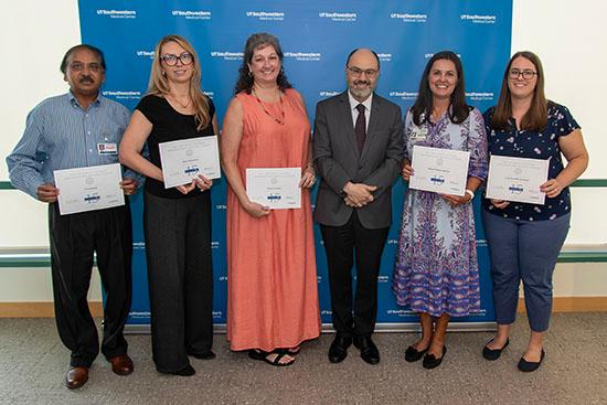 Six people stand in a row holding up their service certificates.