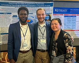 Moez Bashir (left), Chardrick Lane (center), and Kathy Niu stand in front of a poster at the American Neuropsychiatric Association event in March