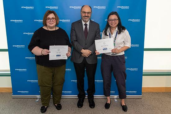 Three people stand in a row holding up their service certificates.