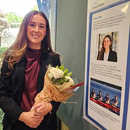 Undergrad student Emory Oakes stands with a bouquet of flowers next to a poster of her presentation