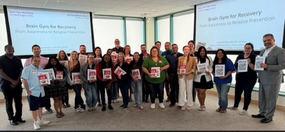 A group of 20 Brain Gym trainers hold up workbooks