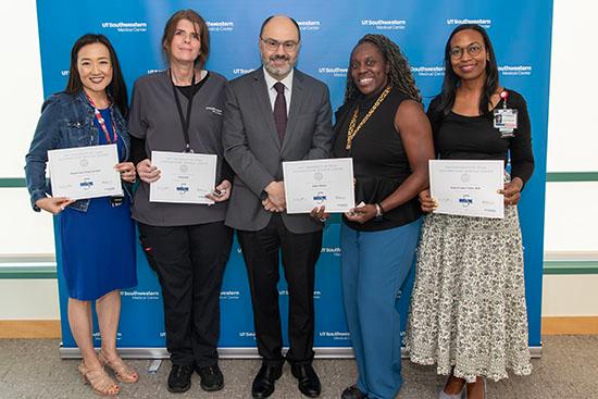 Five people stand in a row holding up their service certificates.