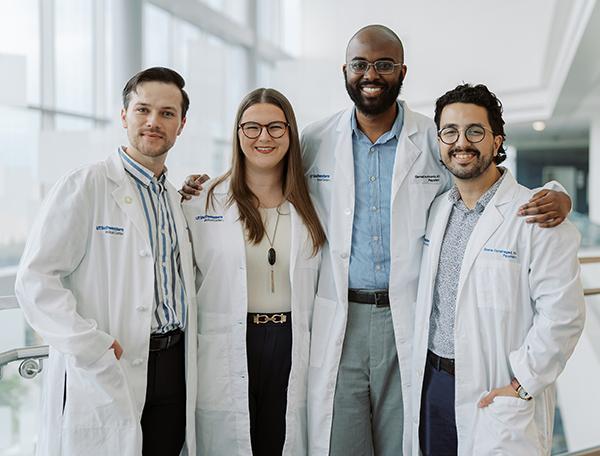 Four people in doctor's coats standing in a row and smiling at the camera