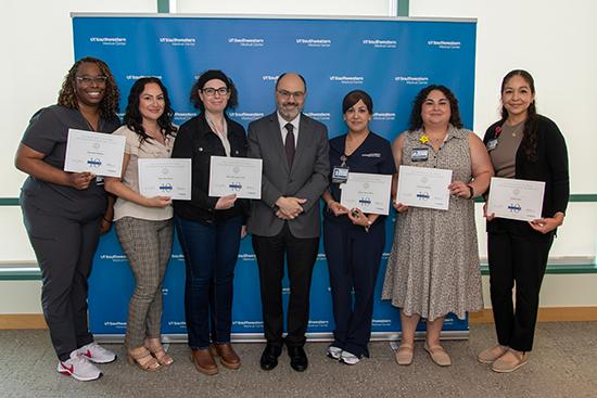 Seven people stand in a row holding up their service certificates.