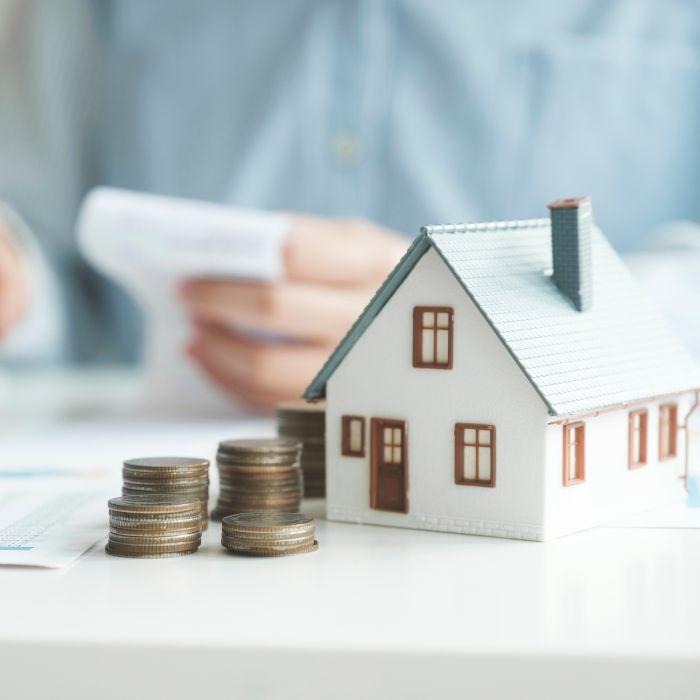 model house with coins and person holding receipt in the background