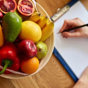Fruit in a bowl hand holding a pencil to write notes on a clipboard