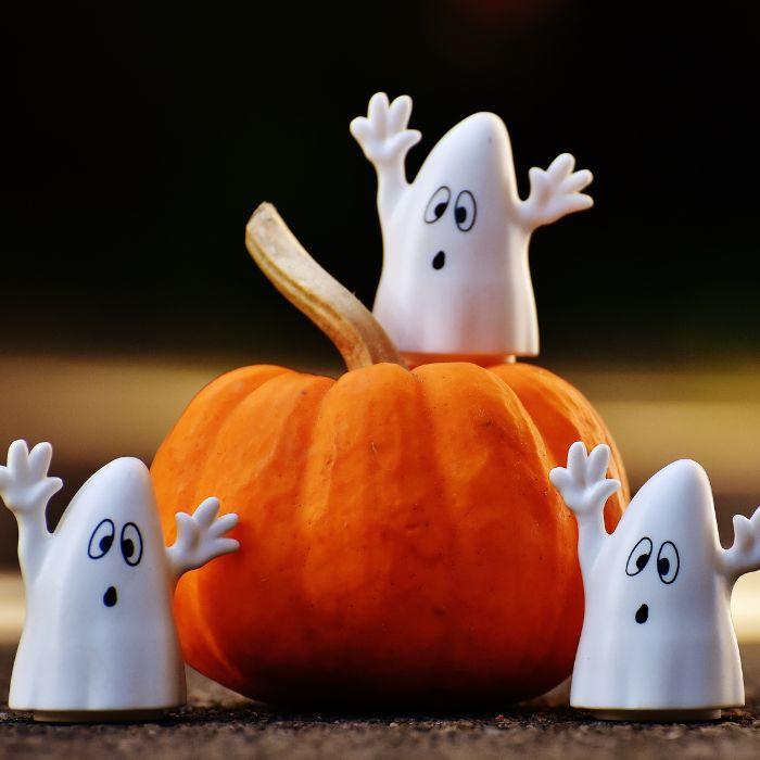 three little ghosts standing around a pumpkin