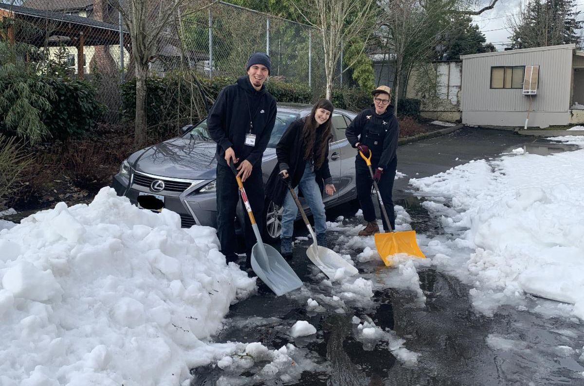 Three MCEM employees with snow shovels dig out a stuck car.