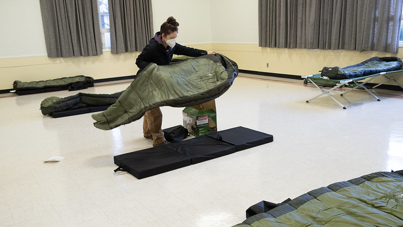 A volunteer placing a sleeping bag onto a pad on the floor of the Mount Scott Community Center emergency warming shelter