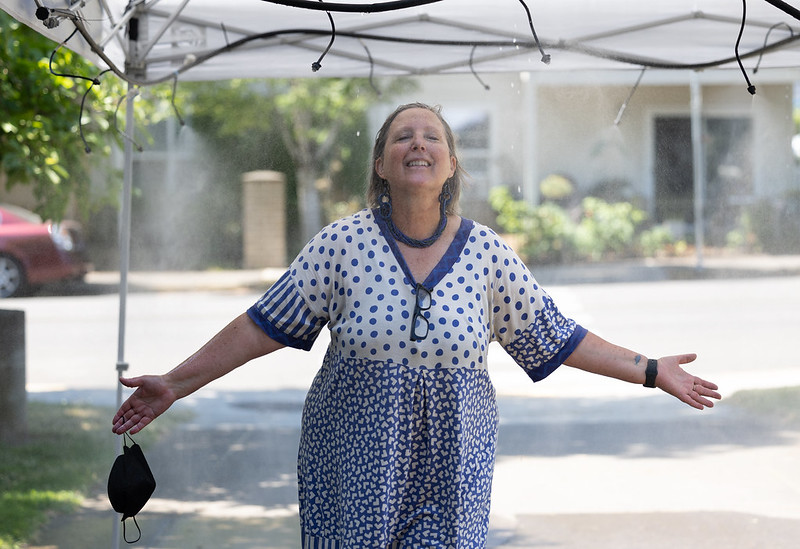 A person in a dress stands underneath a misting station, arms stretched.