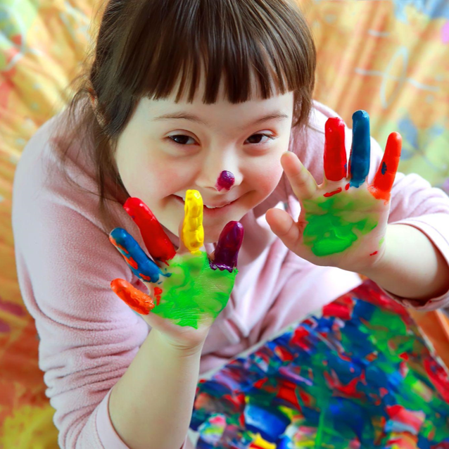 A child holds out their hands covered in finger paint
