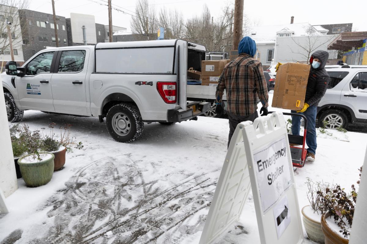 Two people load boxes into a truck outside of an Emergency Shelter with snow on the ground.
