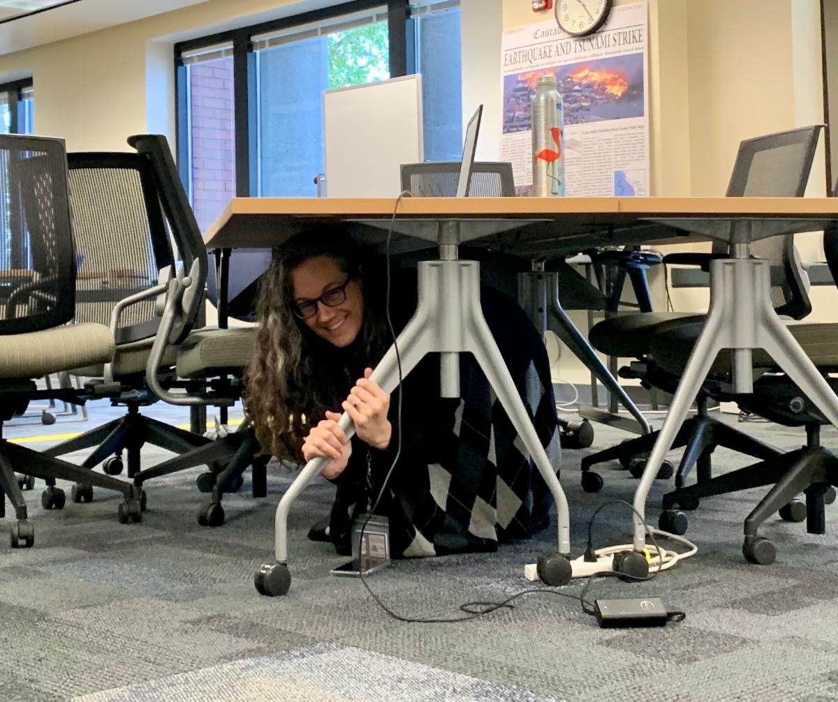 Lydia Ledgerwood-Eberlein practicing "Drop, Cover, and Hold" underneath a table.