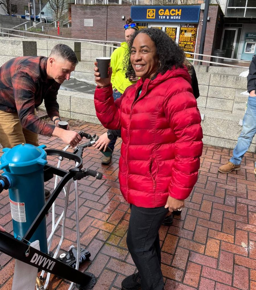 Yvette Osborne of Multnomah County stands smiling with water from the DIVVY filtration system.