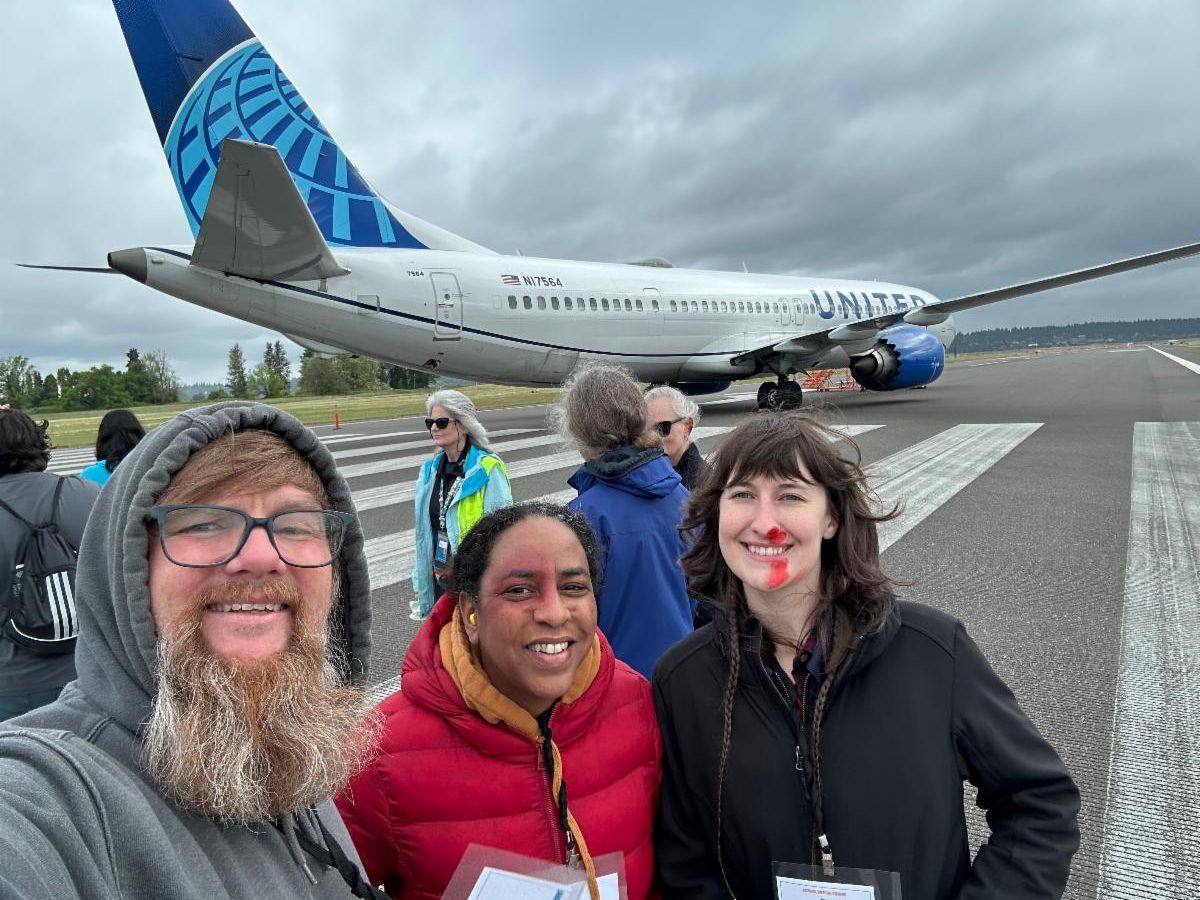 Three MCEM staff members stand smiling in front of a plane on a runway.