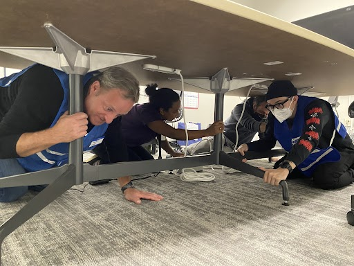 3 MCEM Staff Members take shelter during the Great Shakeout under a table.