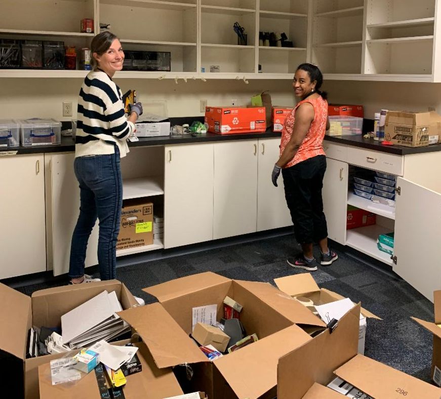 Two Multnomah County Emergency Management staff members standing next to mostly empty shelves with several boxes on the floor