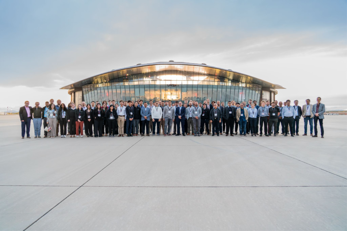 A large group of people standing on a tarmac in front of a modern glass building.