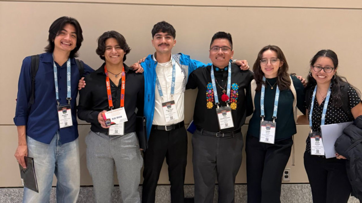 Six people standing together, smiling, wearing conference lanyards.