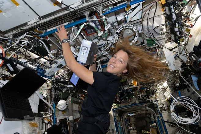 Sophie Adenot floating in microgravity aboard a space station with equipment and cables.